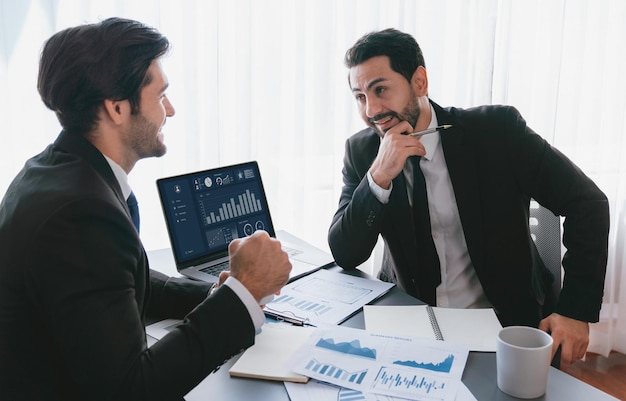 Deux hommes en costume sont assis à un bureau, l'un d'eux regarde un écran qui dit "développez votre entreprise"