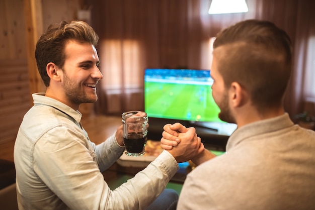 Les deux hommes heureux avec une bière regardent un football et une poignée de main