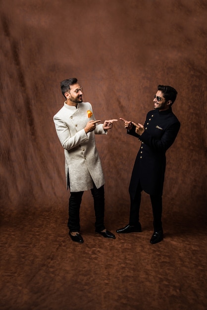 Deux hommes indiens portent des vêtements ethniques ou traditionnels, des mannequins masculins avec sherwani ou Kurta Pyjama, assis et posant sur une bergère ou un canapé sur fond marron grunge, mise au point sélective