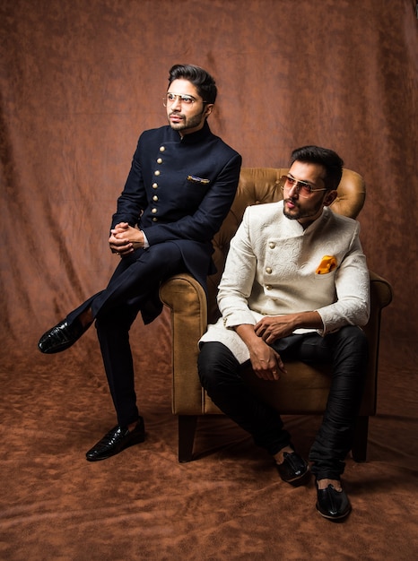 Deux hommes indiens portent des vêtements ethniques ou traditionnels, des mannequins masculins avec sherwani ou Kurta Pyjama, assis et posant sur une bergère ou un canapé sur fond marron grunge, mise au point sélective