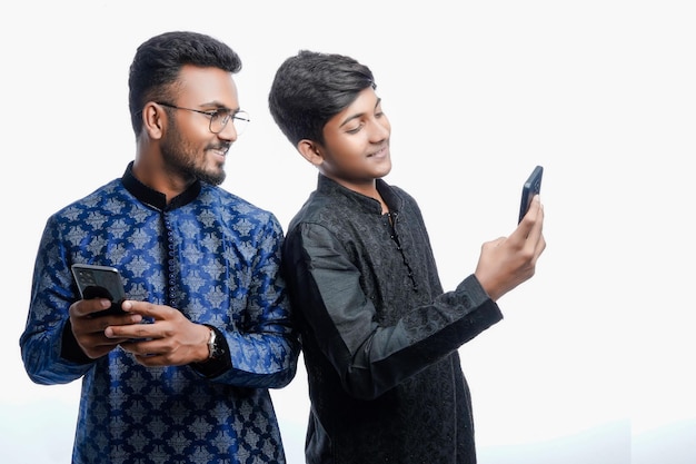 Deux hommes indiens vêtus de vêtements traditionnels et utilisant des téléphones et se regardant l'écran des téléphones de l'autre isolé sur fond blanc