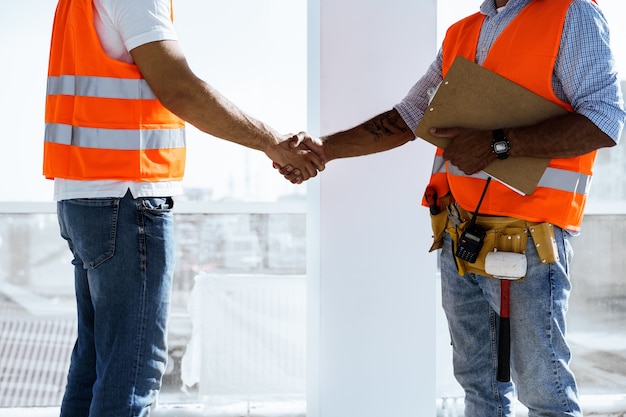 Deux hommes ingénieurs en vêtements de travail se serrant la main contre le chantier de construction