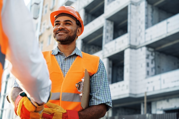 Photo deux hommes ingénieurs en vêtements de travail se serrant la main contre le chantier de construction