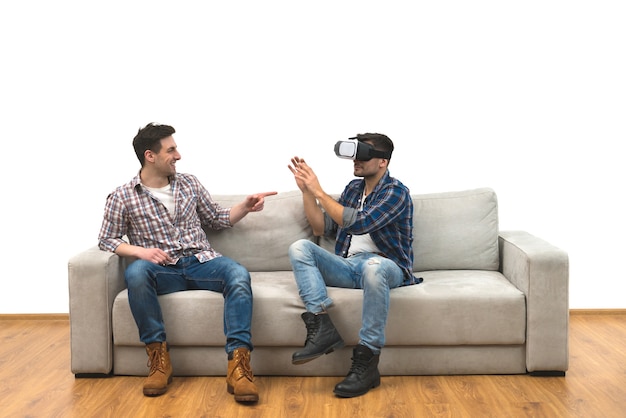 Les deux hommes avec des lunettes virtuelles s'amusent sur un canapé sur un fond de mur blanc