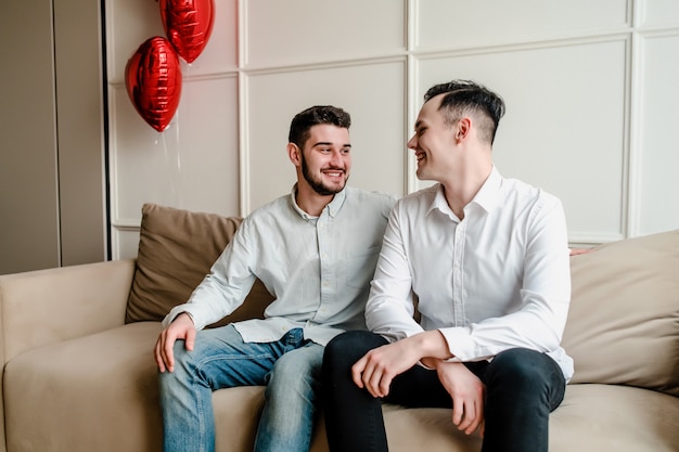 Deux hommes à la maison avec des ballons en forme de coeur sur canapé