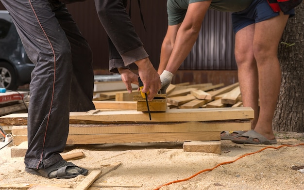 Deux hommes méconnaissables portant des sandales coupant des planches de bois sur un chantier de construction informel d'une nouvelle maison