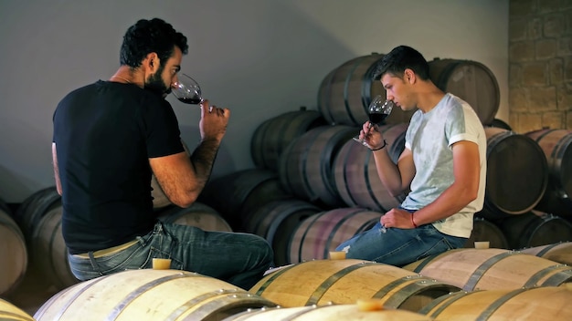 Deux hommes sont assis sur un canapé, dont l'un tient un verre de vin.