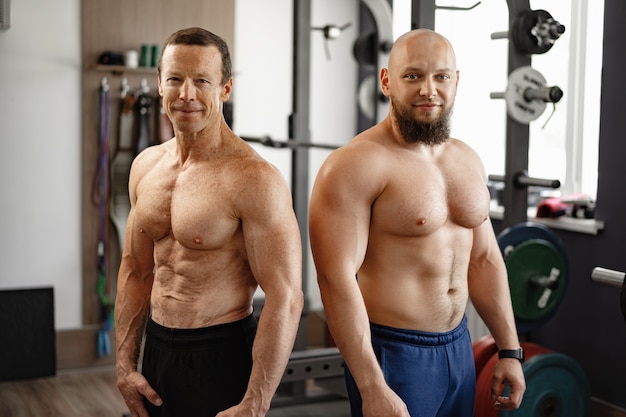 Deux hommes torse nu debout dans une salle de sport jeune homme et son père senior font de l'exercice ensemble dans une salle de sport