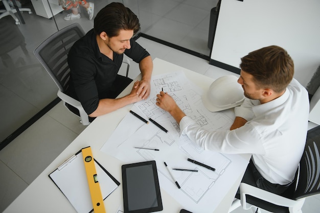 Deux ingénieurs travaillant ensemble et utilisant une tablette numérique à la recherche d'un plan directeur et d'une analyse avec un plan architectural sur le bureau