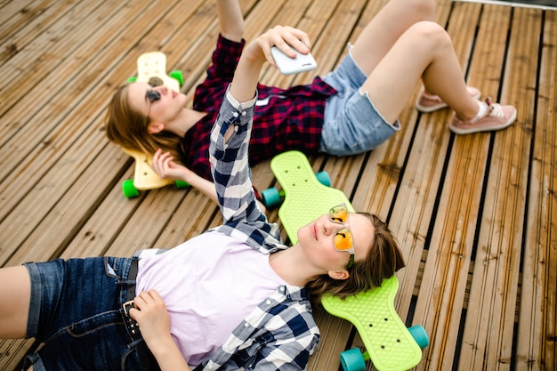 Deux jeune fille en tenue hipster faisant selfie en position couchée avec sur une jetée en bois.