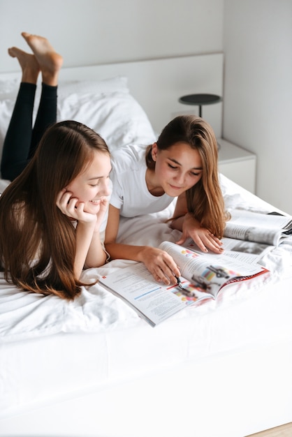 Deux jeunes adolescentes gaies portant sur le lit, magazine de lecture