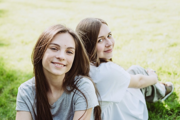 Photo deux jeunes adolescentes heureuses se reposent dans le parc sur l'herbe verte. amitié féminine. mise au point sélective douce.