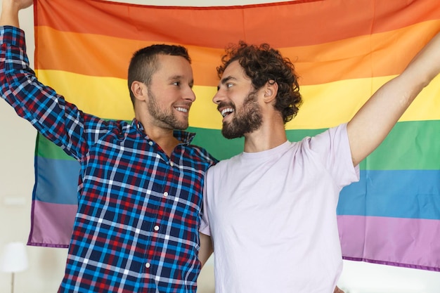 Deux jeunes amants gays se regardant affectueusement Deux jeunes amants se tenant ensemble contre un drapeau de fierté Affectueux jeune couple gay partageant un moment romantique ensemble