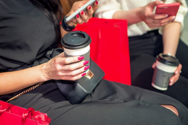 Deux jeunes amies utilisent des smartphones et boivent du café, assis dans le café.