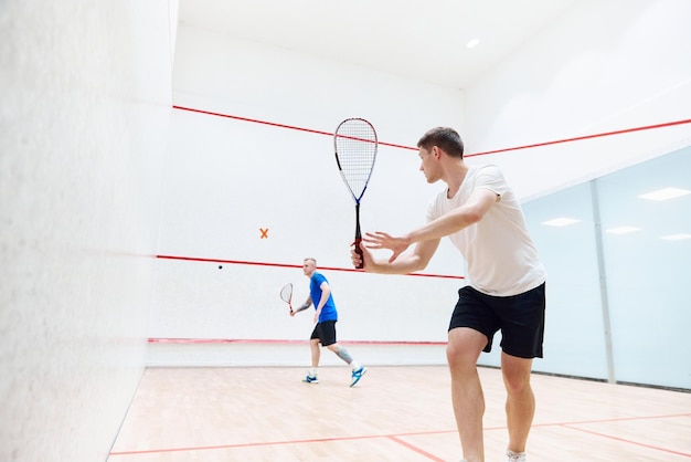 Deux jeunes amis hommes concentrés et sportifs jouant au squash ensemble sur un court de squash faisant de l'exercice