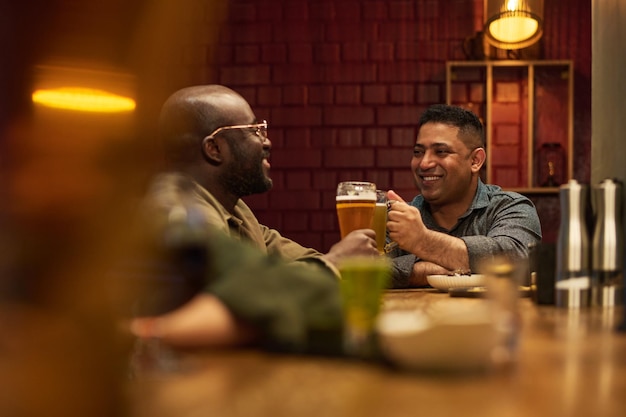 Deux jeunes amis interculturels heureux qui claquent des verres de bière mousseuse.