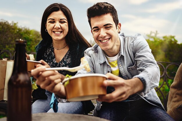 Deux jeunes amis mangent joyeusement des aliments sains dans des récipients en papier recyclables un week-end de printemps