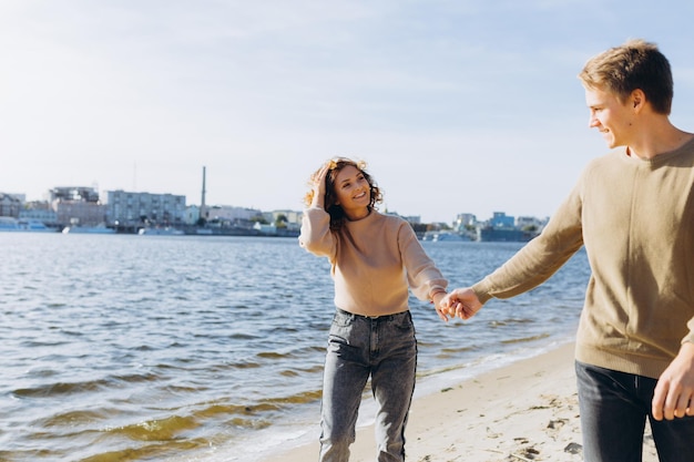 Deux jeunes amoureux courant sur la plage Ils se sourient Beau couple Beach Feeling Habillez-vous en pull