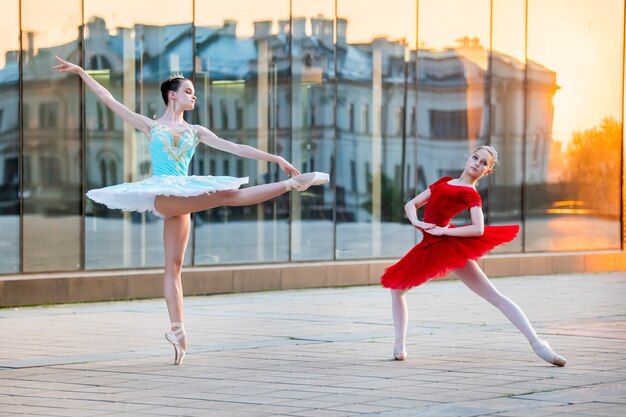 Deux jeunes ballerines dans un tutu rouge et bleu vif dansent sur fond de reflet du coucher de soleil de la ville