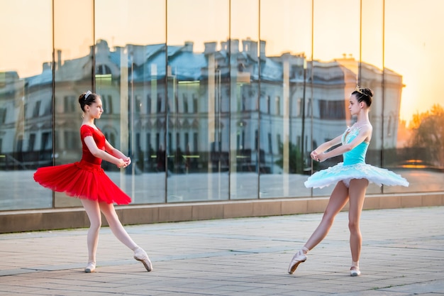 Deux jeunes ballerines dans un tutu rouge et bleu vif dansent sur fond de reflet du coucher de soleil de la ville