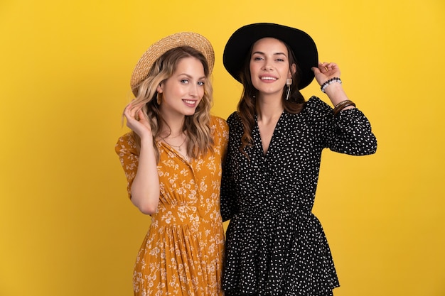 deux jeunes belles femmes amies ensemble isolées sur jaune en robe noire et jaune et chapeau tendance boho élégant