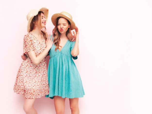 Deux jeunes belles femmes hipster brune souriante dans des robes d'été à la mode Sexy femmes insouciantes posant près du mur rose Modèles positifs s'amusant Gai et heureux En chapeaux