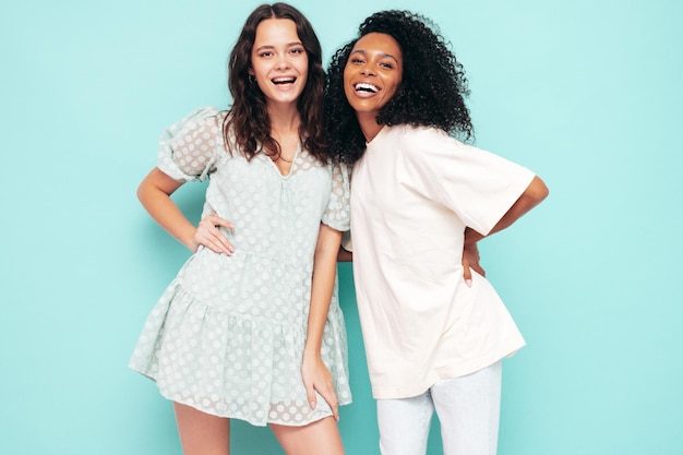 Deux jeunes belles femmes hipster internationales souriantes dans des vêtements d'été à la mode Sexy femmes insouciantes posant près du mur bleu en studio Modèles positifs s'amusant Concept d'amitié