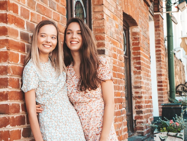 Deux jeunes belles femmes hipster souriantes dans des robes d'été à la modeFemmes insouciantes sexy posant dans la rue Modèles purs positifs s'amusant au coucher du soleil étreignant et devenant fous