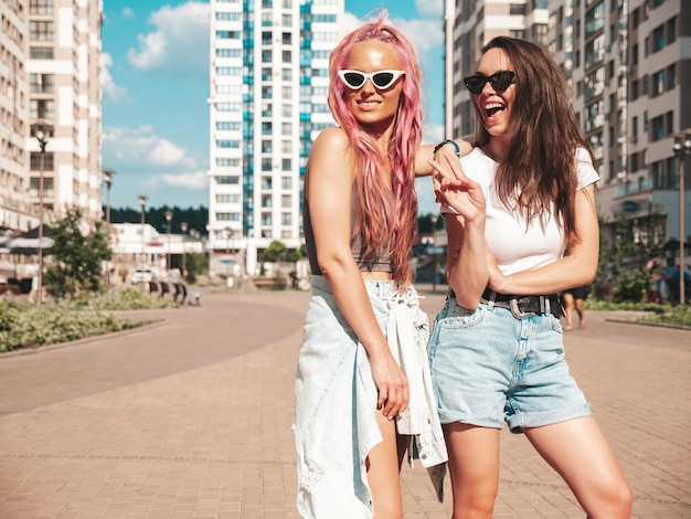 Deux jeunes belles femmes hipster souriantes dans des vêtements d'été à la mode. Femmes insouciantes sexy posant dans la rue avec des cheveux roses. Modèles purs positifs s'amusant au coucher du soleil. Gai et heureux