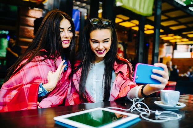 Deux jeunes et belles filles assises à la table et faisant un selfie au café