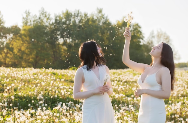 Deux jeunes belles filles sur le pré avec des pissenlits au coucher du soleil