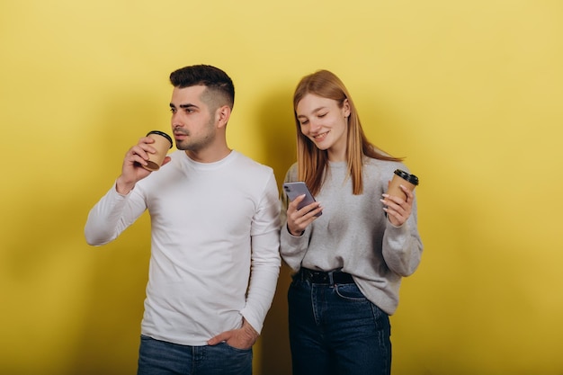 Deux jeunes belles personnes fille et mec debout sur un fond jaune Ils boivent du café