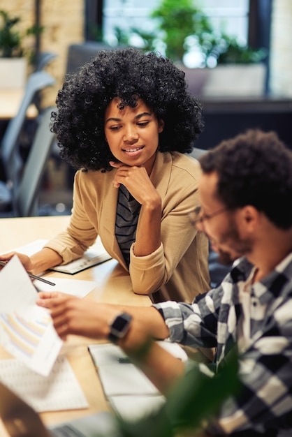 Deux jeunes collègues divers analysant le rapport de vente tout en travaillant ensemble au bureau