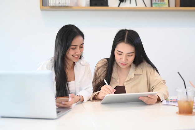 Deux jeunes collègues femmes assises au bureau parlant d'idées de démarrage de projet et discutant de la stratégie de croissance au bureau.