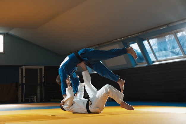 Deux jeunes combattants de judo en kimono s'entraînant aux arts martiaux dans la salle de gym avec expression, en action et en mouvement