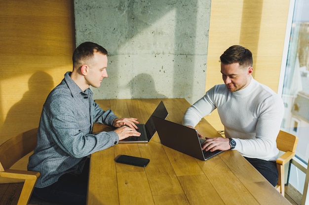 Deux jeunes confiants sont assis ensemble à une table et l'un d'eux pointe un ordinateur portable Travaillez sur un nouveau projet Des collègues qui réussissent travaillent ensemble au bureau