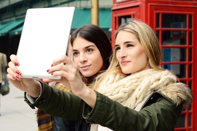 Deux jeunes copines prennent selfie avec tablette.