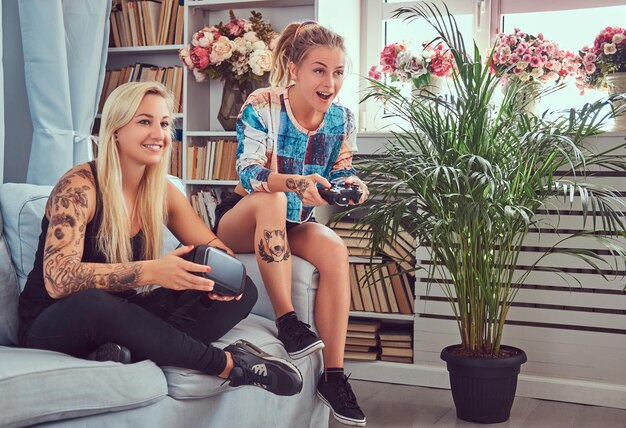 Deux jeunes copines en vêtements décontractés jouent à des jeux vidéo à la maison.