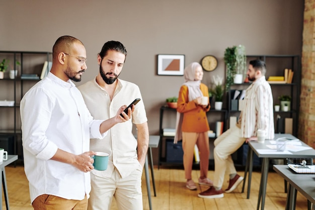 Deux jeunes courtiers confiants en vêtements décontractés discutant d'un tableau sur un smartphone