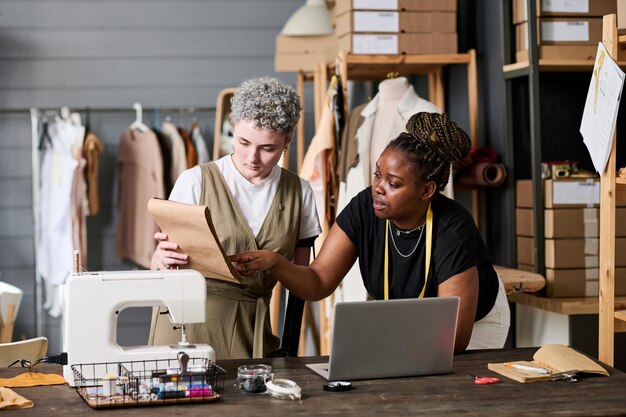 Deux jeunes couturières interculturelles discutant d'un nouveau croquis de tenue vestimentaire