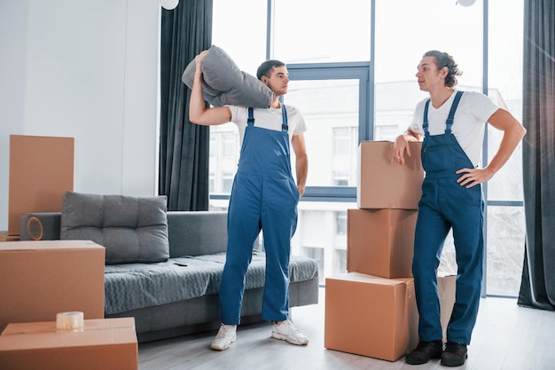 Deux jeunes déménageurs en uniforme bleu travaillent à l'intérieur de la pièce.