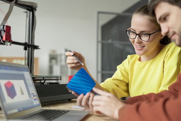 Deux Jeunes Designers Contemporains Discutant D'un Objet En Plastique Bleu Devant Un Ordinateur Portable Après L'avoir Imprimé Sur Une Imprimante 3d