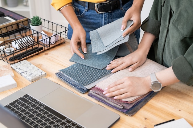 Deux jeunes designers créatifs contemporains de l'intérieur choisissant des échantillons de textile pour les meubles pour appartement ou maison moderne en face d'un ordinateur portable