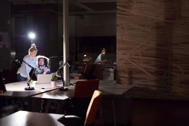 Deux jeunes designers travaillent sur un nouveau projet dans le bureau de nuit en utilisant la technologie moderne