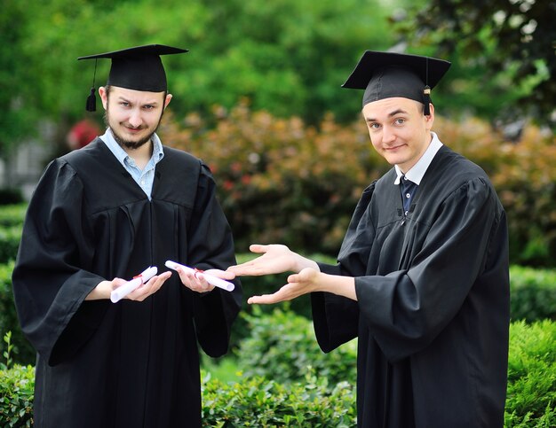 Deux jeunes diplômés universitaires en robes et chapeaux carrés sont heureux de recevoir un diplôme