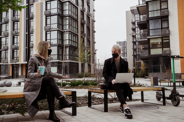 Deux jeunes discutent de quelque chose d'intéressant, assis sur des bancs et gardant la distance