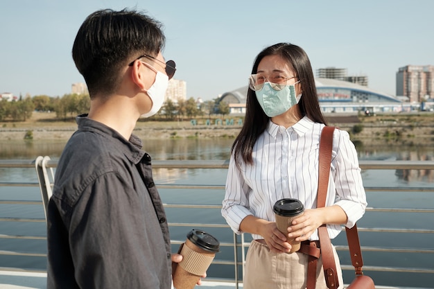 Deux jeunes employés chinois portant des masques de protection discutent des points de travail tout en se tenant au bord de la rivière