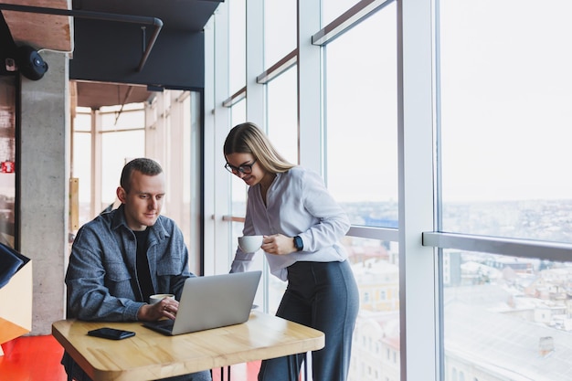 Deux jeunes entrepreneurs derrière un ordinateur portable regardent une présentation au bureau et discutent du plan de développement de l'entreprise