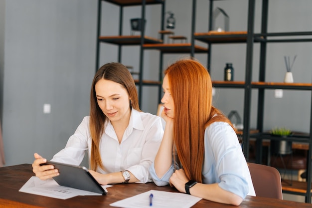 Deux jeunes femmes d'affaires concentrées travaillant à l'aide d'une tablette numérique ayant une réunion assise au bureau avec des documents de travail au bureau Partenaires commerciaux utilisant un ordinateur à écran tactile pour la discussion de projet