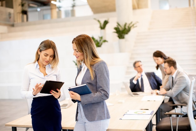 Deux jeunes femmes d'affaires regardant les résultats financiers sur une tablette numérique devant leur équipe au bureau